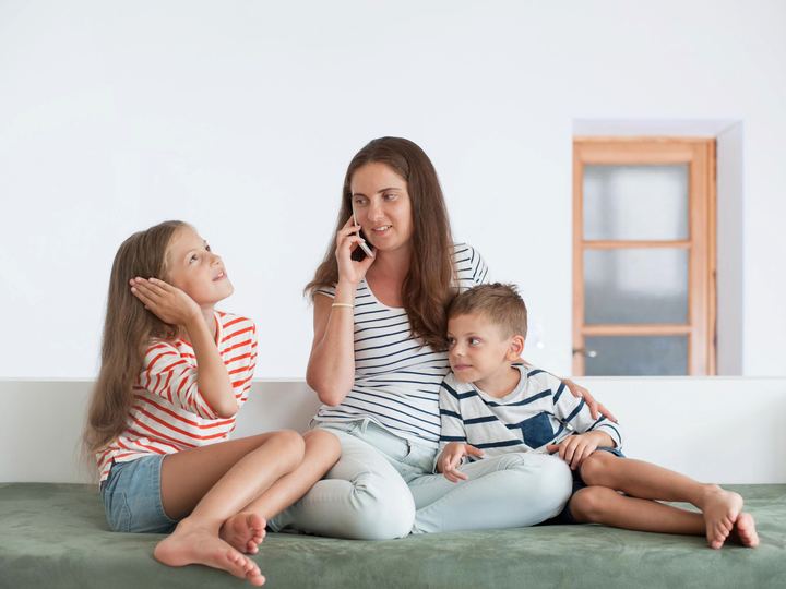 A mum on the phone at home while her two children sit beside her