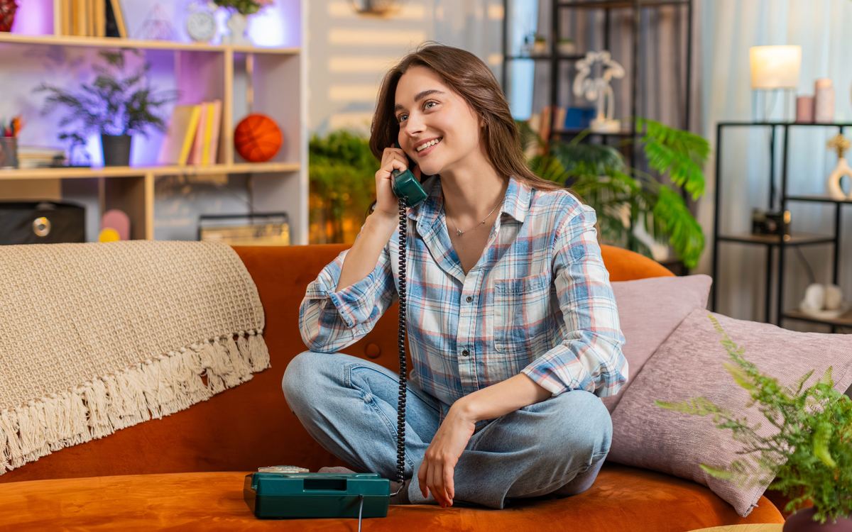 A smiling woman chatting on her home phone, sitting on the sofa